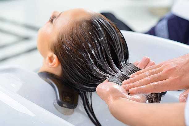 Person receiving shampoo treatment at a salon, hands massaging scalp.