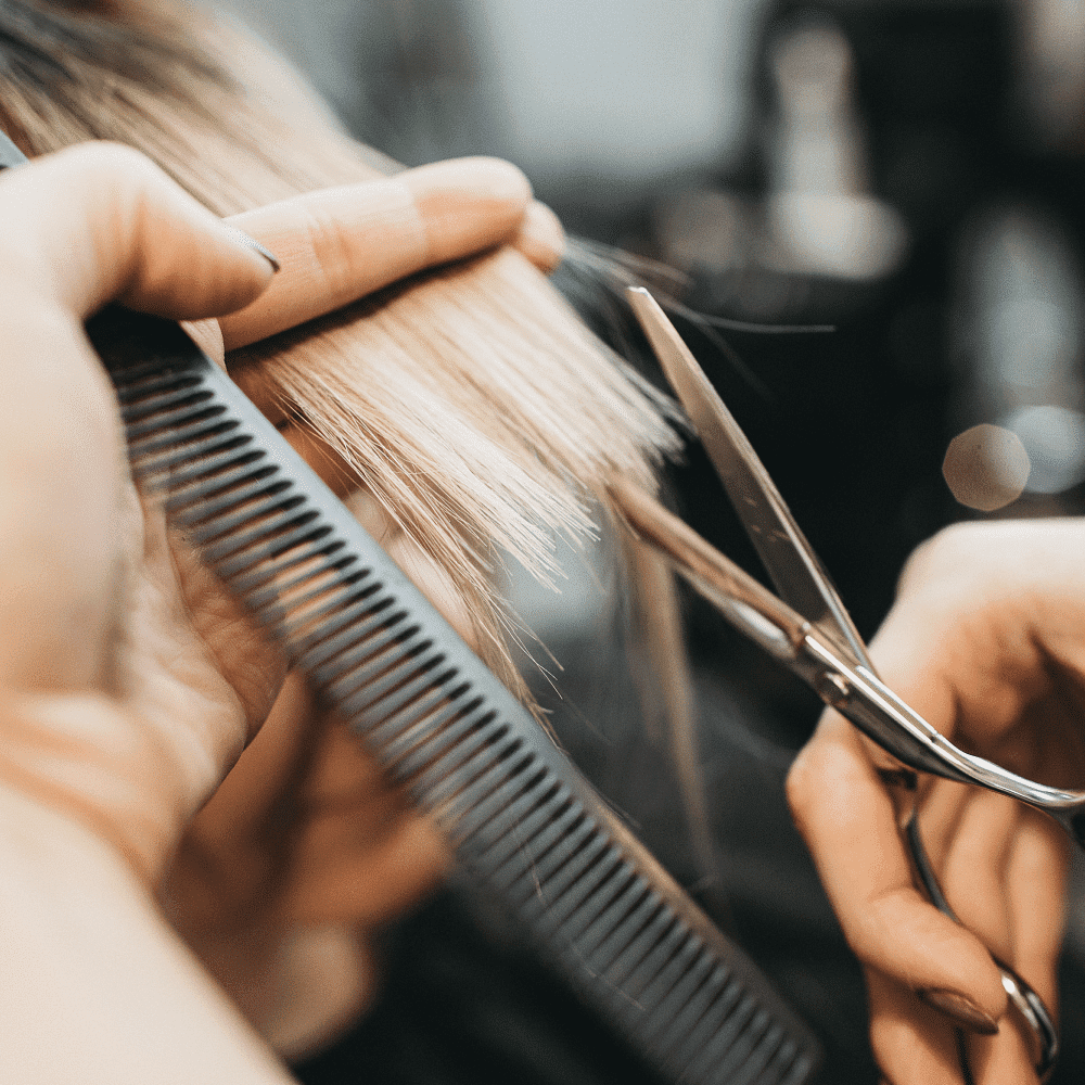 Hairdresser cutting blonde hair with scissors and comb in a salon.
