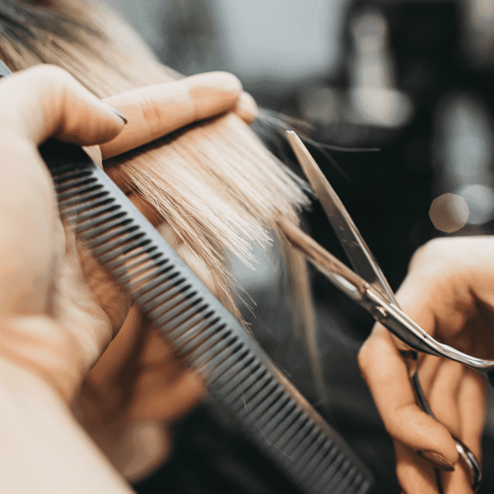 Hairdresser cutting blonde hair with scissors and comb in a salon.